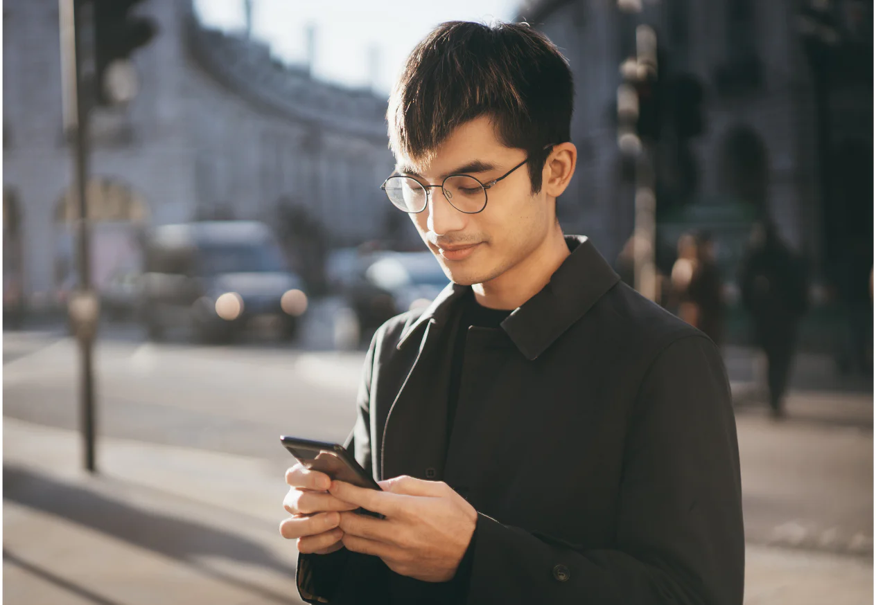 Man with glasses using smartphone on a city street in daylight